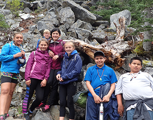 Group of children taking a break from backpacking up the trail with a backdrop of boulders